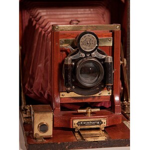May include: Antique wooden Century brand camera with a bellows system, a lens, and a brass plate with the word "Century" on it.