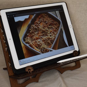 May include: A wooden tablet stand with a carved design, holding a white tablet displaying a recipe for sweet potato casserole. A white stylus is resting on the stand.