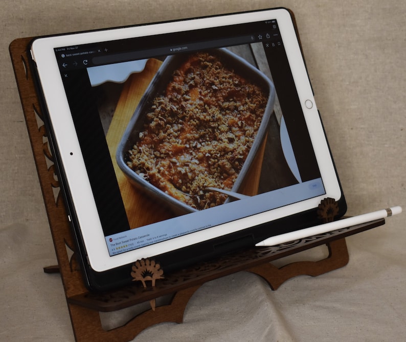 May include: A wooden tablet stand with a carved design, holding a white tablet displaying a recipe for sweet potato casserole. A white stylus is resting on the stand.