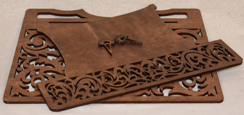 May include: A set of three unfinished wooden pieces with intricate cut-out designs. The pieces are stacked on top of each other and have a brown color.