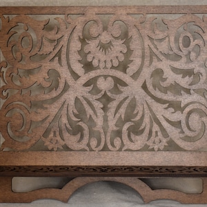 May include: A wooden music stand with a decorative, intricate, laser-cut design. The stand has a shelf and a curved base.