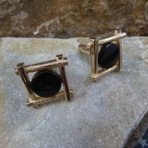 May include: A pair of gold cufflinks with black circular stones set in a geometric frame.