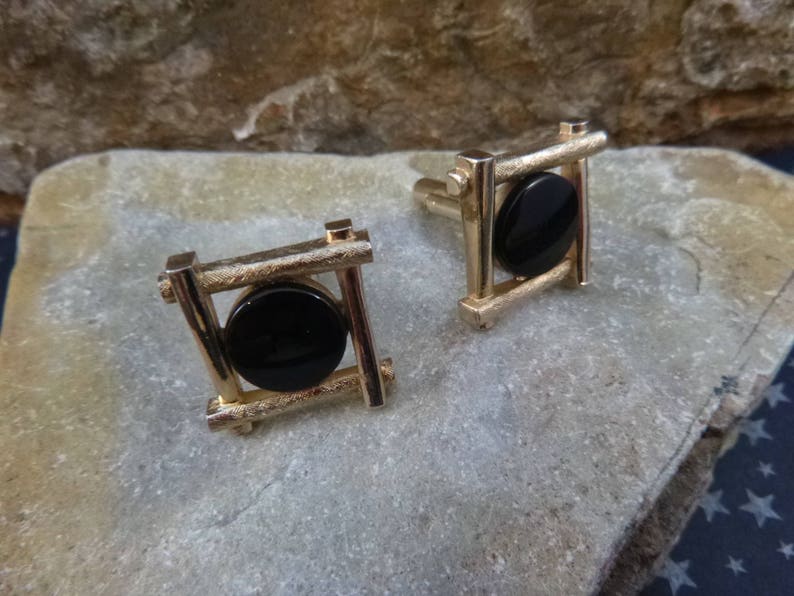 May include: A pair of gold cufflinks with black circular stones set in a geometric frame.