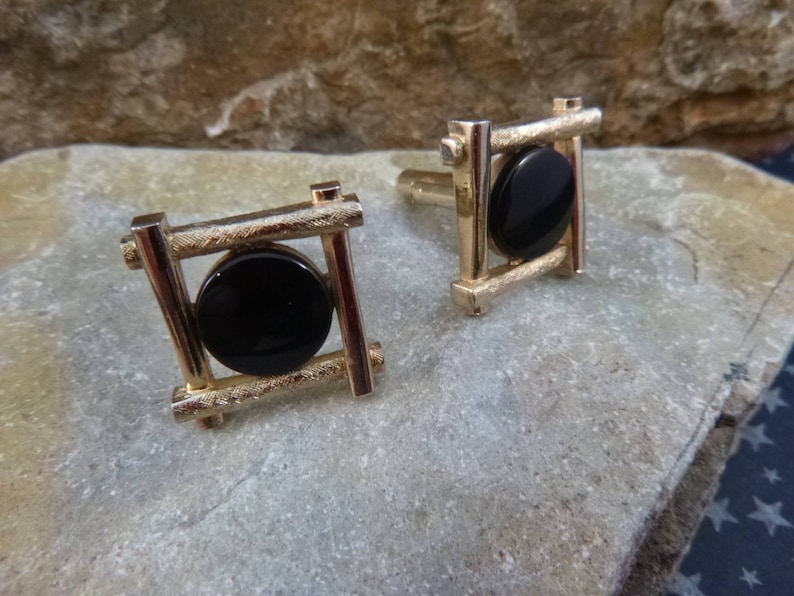 May include: A pair of gold cufflinks with black onyx stones set in a geometric design.