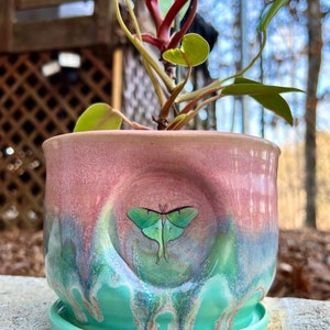 May include: A green and pink ceramic planter with a green luna moth design. The planter has a drip glaze and a matching saucer.