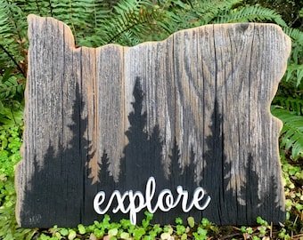 May include: A wooden sign shaped like the state of Oregon with a black silhouette of trees and the word "explore" painted in white.