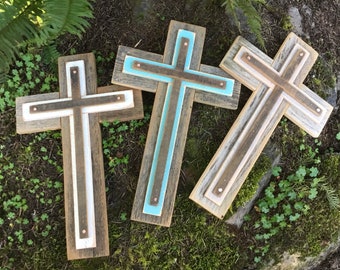 May include: Three wooden crosses with different colored accents. The crosses are made of reclaimed wood and have a rustic look. The crosses are all different sizes and have different colored accents. The crosses are all standing on a bed of green moss.
