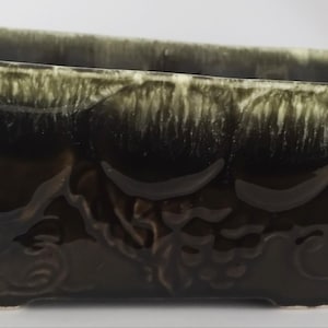May include: A rectangular, dark green ceramic planter with a glossy finish. The planter has a textured design with a grape motif on the front and sides. The top edge has a lighter green, textured trim.