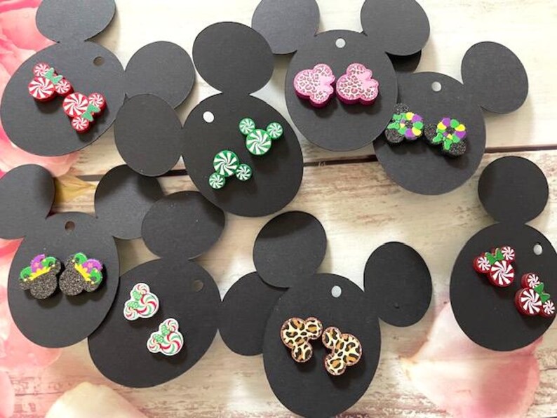May include: Assortment of colorful, whimsical earrings displayed on black Mickey Mouse-shaped cards. The earrings feature various designs, including candy canes, Mickey Mouse heads, and animal prints.