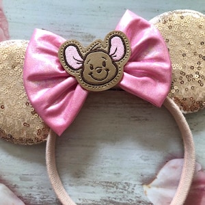 May include: Pink and gold sequined Minnie Mouse ears with a brown embroidered character in the center.
