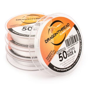 May include: A stack of clear plastic spools containing white DragonThread for jewelry-making. Each spool features an orange and black label with the text DragonThread, Crystal, 50 meters, size 6, and information about the polyethylene fiber.