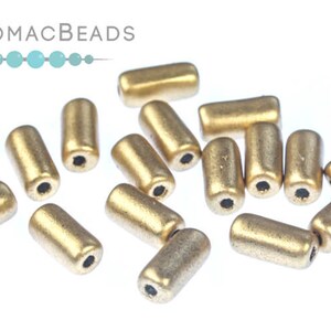 May include: A group of gold-colored glass beads in a cylindrical shape. The beads have a matte finish and are scattered on a white surface.