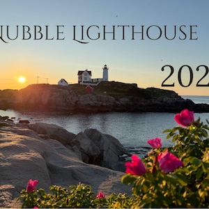 May include: A calendar image featuring Nubble Lighthouse on a rocky island at sunset with bright pink wild roses in the foreground. The text NUBBLE LIGHTHOUSE and 2027 are printed in black against the clear blue sky above the horizon.