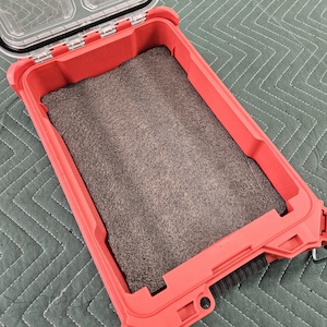 May include: Open red waterproof case with a clear lid. The interior has a dark grey foam insert. The case is designed to protect items from water and impact. The case is open, revealing the interior.