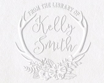 Puede incluir: Un sello en relieve blanco con el texto "From the Library of Kelly Smith" en un círculo rodeado de cuernos de ciervo y flores. También se muestra un sello autoentintado negro y plateado.