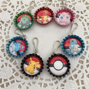 May include: Seven colorful bottle cap charms featuring different Pokemon characters. Each charm has a silver clip attached. The charms are arranged in a circle on a white doily.