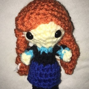 May include: A crocheted doll with long orange hair, blue and black clothing, and large black eyes.