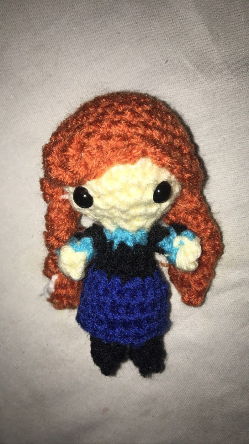 May include: A crocheted doll with long orange hair, blue and black clothing, and large black eyes.