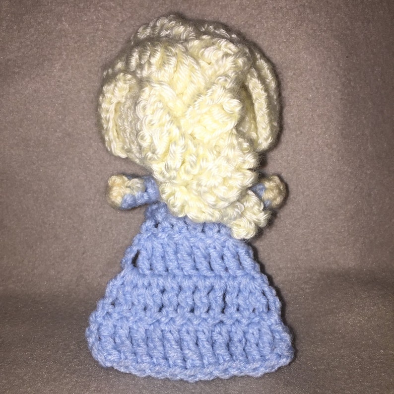 May include: A crocheted doll with a light blue dress and a yellow braided hairstyle.