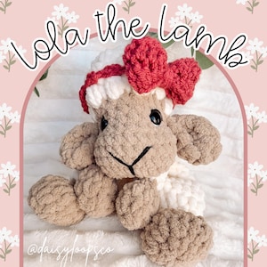 May include: A handmade, plush lamb toy in shades of beige and white, adorned with a red bow. The lamb has black eyes and a stitched black mouth. The text "Lola the Lamb" is written above the lamb. The toy is made of soft, textured yarn.