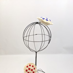 May include: Two felt pie-shaped ornaments with different coloured patterns. The ornaments are displayed on a wire hat stand. The pie on top has a blue and white checked pattern. The pie on the bottom has a red and white checked pattern.