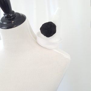 May include: A white felt shoulder pad with a black felt circle in the center. The shoulder pad is on a white dress form.