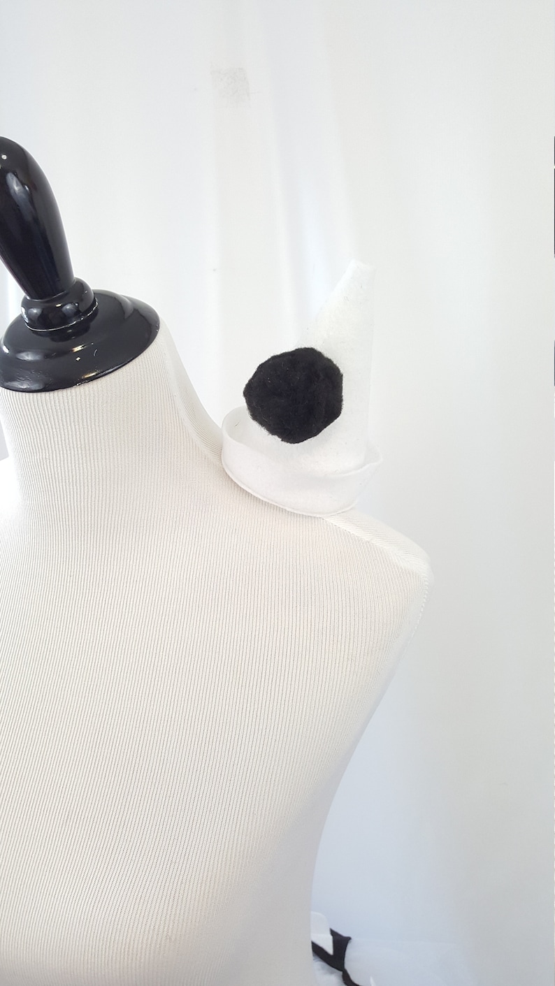 May include: A white felt shoulder pad with a black felt circle in the center. The shoulder pad is on a white dress form.