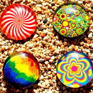 May include: Four round glass paperweights with different colorful designs. One has a red and white spiral pattern, another has a green, yellow, and blue floral pattern, another has a rainbow tie-dye pattern, and the last one has a pink, yellow, and blue flower pattern.