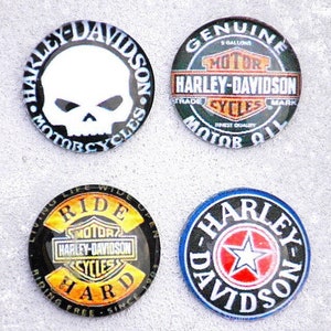 May include: Four round Harley Davidson motorcycle themed buttons. The buttons are black with white, red, and yellow accents. The buttons feature different logos and text, including "Harley-Davidson", "Motorcycles", "Ride Hard", and a skull.