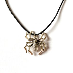 Puede incluir: Un collar con un colgante de araña de plata en un cordón negro.