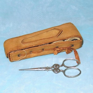 May include: A brown leather sewing kit with a lace closure and a pair of silver scissors. The kit contains spools of thread.