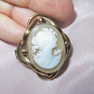 Op de afbeelding: Een gouden cameo broche met een witte cameo van een vrouwenprofiel. De cameo is gezet in een gouden ovale lijst met een gedraaid ontwerp.