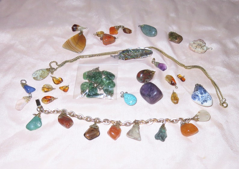 May include: A collection of gemstone pendants, some on chains, some on a bracelet, and some loose. The gemstones are various colors, including green, blue, purple, orange, and brown.