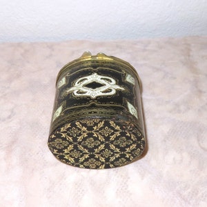 May include: A black cylindrical box with a gold and white floral design. The box has a hinged lid and a brass clasp.