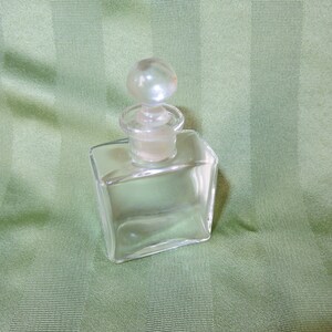 May include: A clear glass bottle with a round glass stopper. The bottle is square shaped and has a smooth surface.