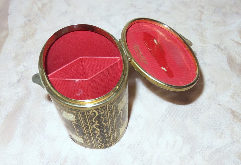 May include: A small, round, black and gold trinket box with a red velvet interior. The box has a hinged lid and is divided into three compartments.