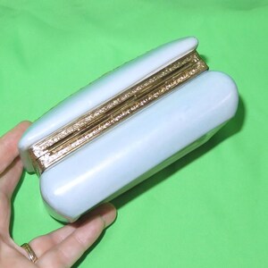 May include: A light blue rectangular box with a gold trim around the edges. The box is closed and the lid is slightly ajar.