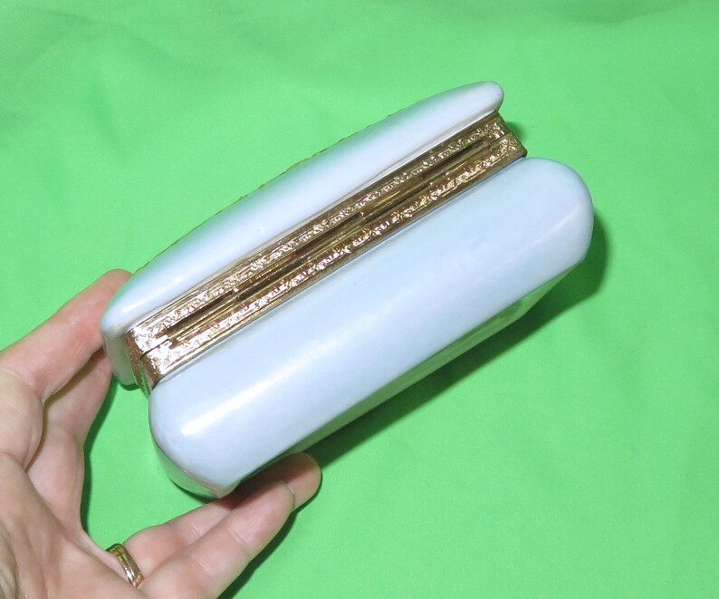 May include: A light blue rectangular box with a gold trim around the edges. The box is closed and the lid is slightly ajar.