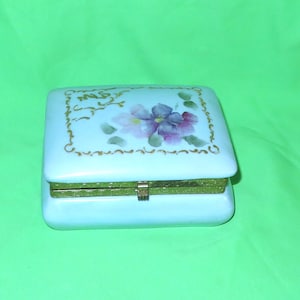 May include: A light blue porcelain trinket box with a hinged lid. The lid is decorated with a gold floral design and the words "Mrs." in gold lettering.