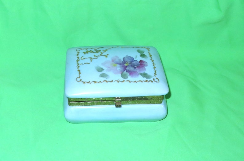 May include: A light blue porcelain trinket box with a hinged lid. The lid is decorated with a gold floral design and the words "Mrs." in gold lettering.