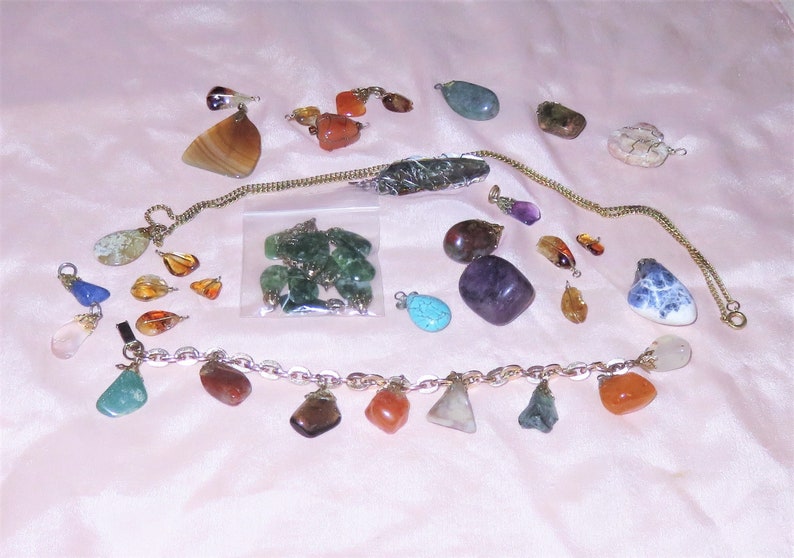 May include: A collection of gemstone pendants and charms, including amethyst, agate, amber, turquoise, and jade. The stones are various shapes and sizes, and some are strung on a gold chain.