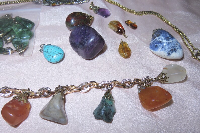 May include: A gold chain necklace with various gemstone pendants, including turquoise, amethyst, carnelian, and clear quartz. The necklace is displayed on a pink fabric background.