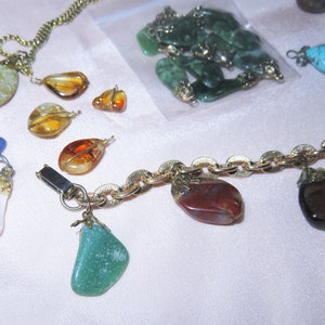 May include: A gold chain necklace with various gemstone charms, including green, blue, brown, pink, and orange. The charms are attached to the chain with gold clasps.