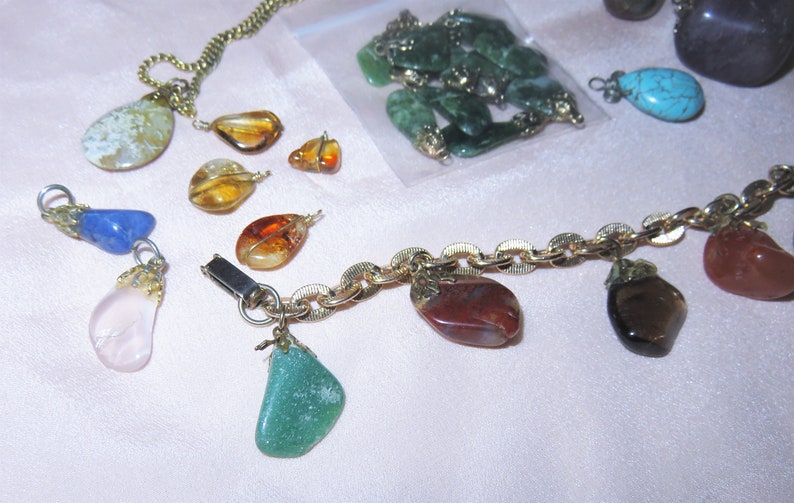 May include: A gold chain necklace with various gemstone charms, including green, blue, brown, pink, and orange. The charms are attached to the chain with gold clasps.