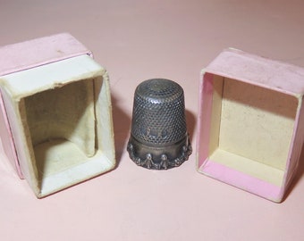 May include: A silver thimble with a decorative edge, in a pink box with a white interior.