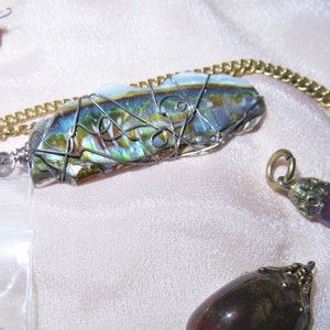 May include: A silver wire wrapped abalone shell pendant on a gold chain. The pendant is iridescent with green, blue, and gold hues.