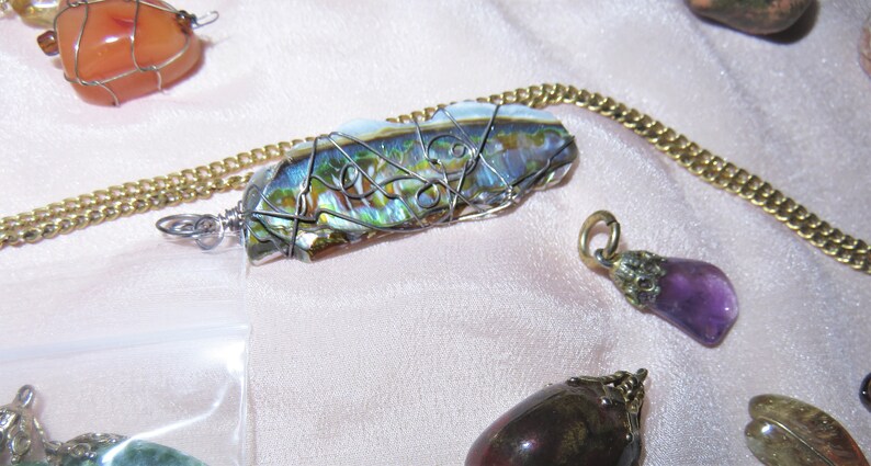 May include: A silver wire wrapped abalone shell pendant on a gold chain. The pendant is iridescent with green, blue, and gold hues.