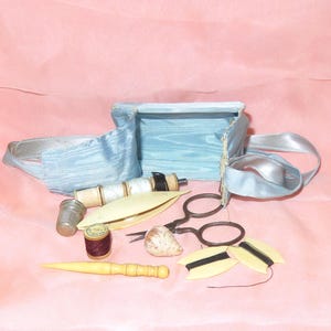 May include: A vintage blue satin sewing kit with a variety of tools, including a thimble, spools of thread, a needle threader, and a pair of scissors.