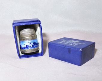 May include: A silver thimble with a blue and white enamel design of windmills and tulips. The thimble is in a blue box with the text "VINTAGE DUTCH THIMBLE" printed on the side.