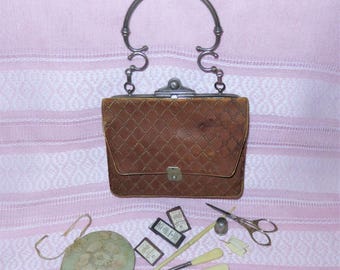 May include: A brown quilted fabric handbag with a silver metal handle and clasp. Included are a round floral pincushion, three small rectangular boxes, a metal thimble, a pair of silver scissors, and four sewing tools with cream handles.